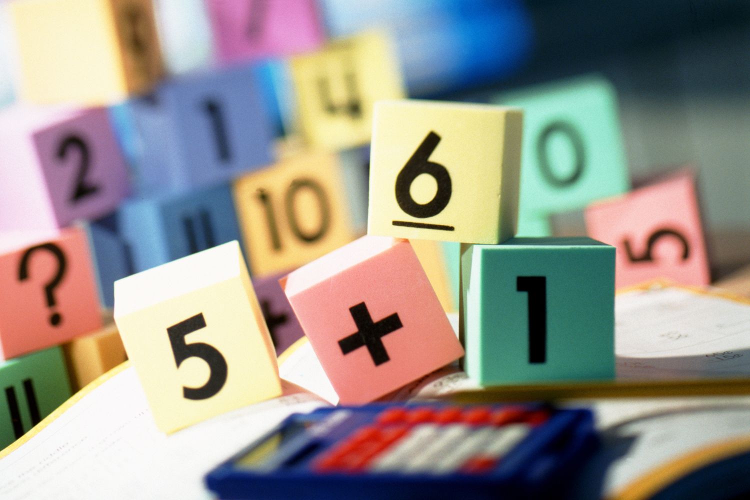 Zdjęcie kolorowych klocków z cyframi. Na pierwszym planie kalkulator.