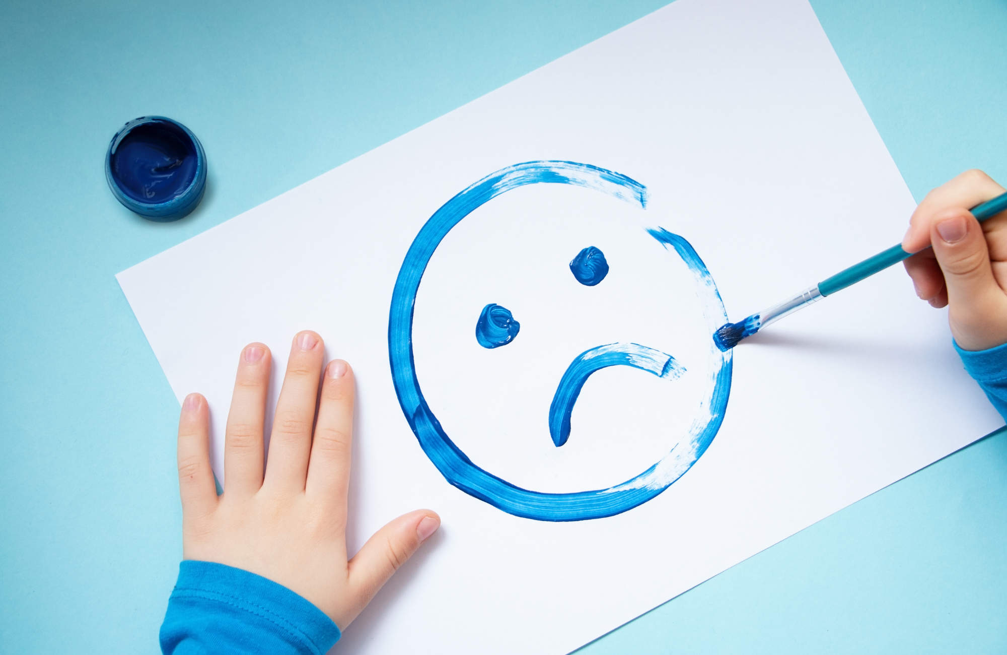 Zdjęcie rysunku przedstawiającego smutną minę. Na brzegach rysunku ręce dziecka.